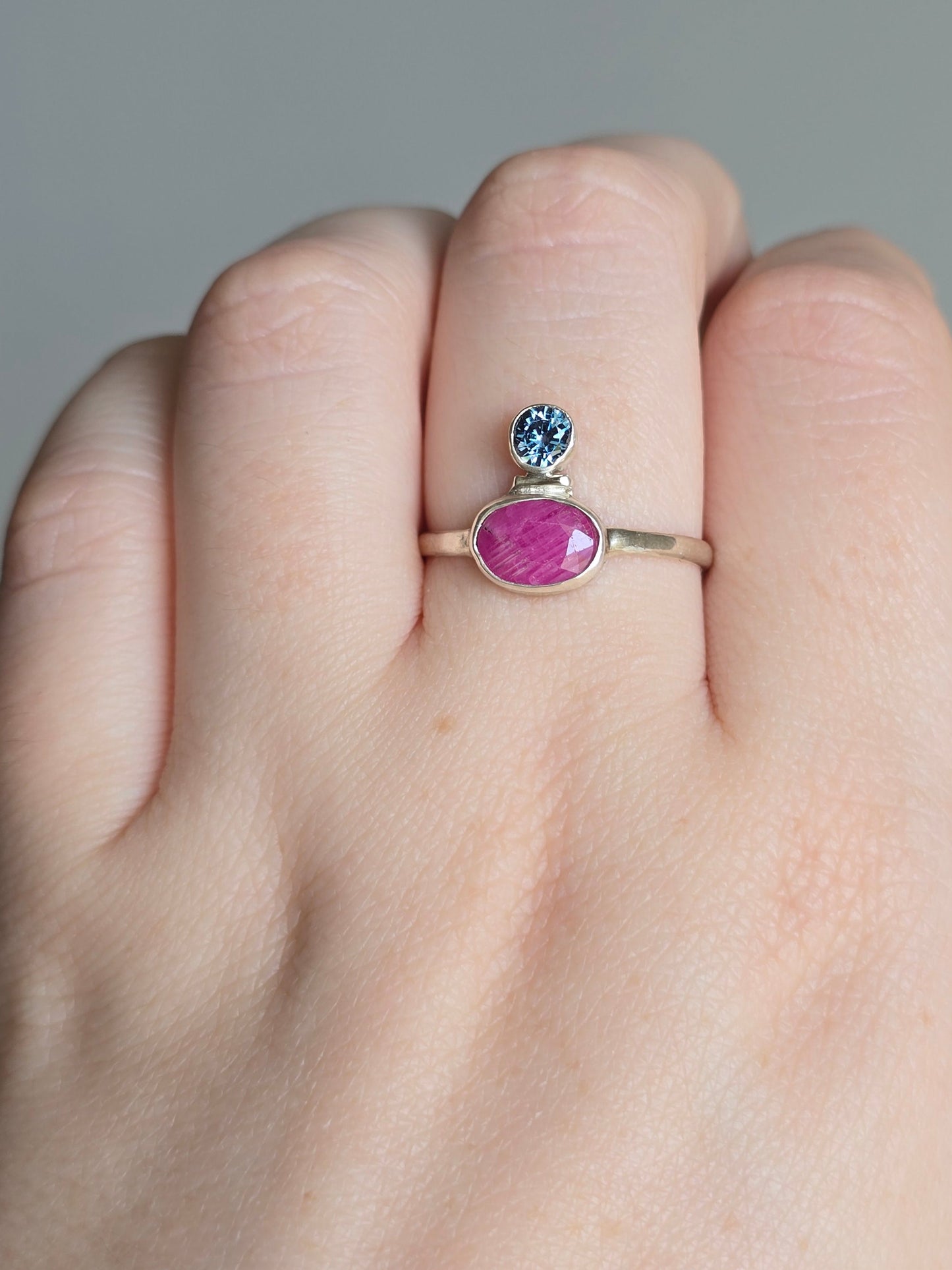 Close-up of a hand wearing a ring with a pink gemstone on a gray background