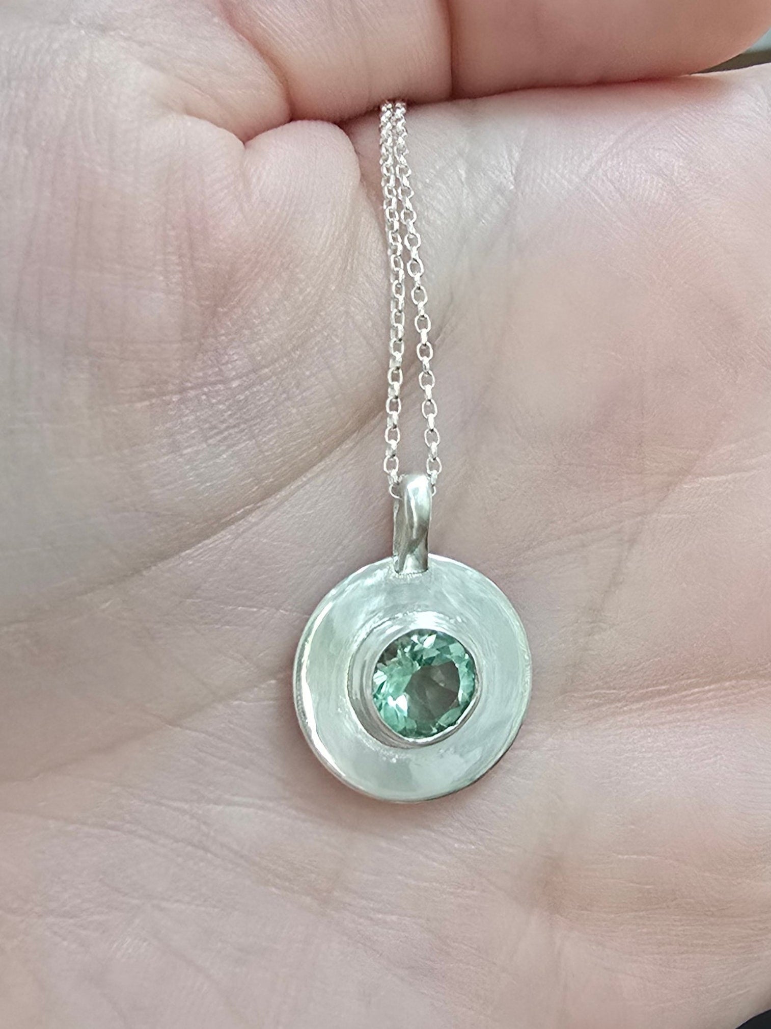 Hand holding a silver necklace with a green gemstone pendant.